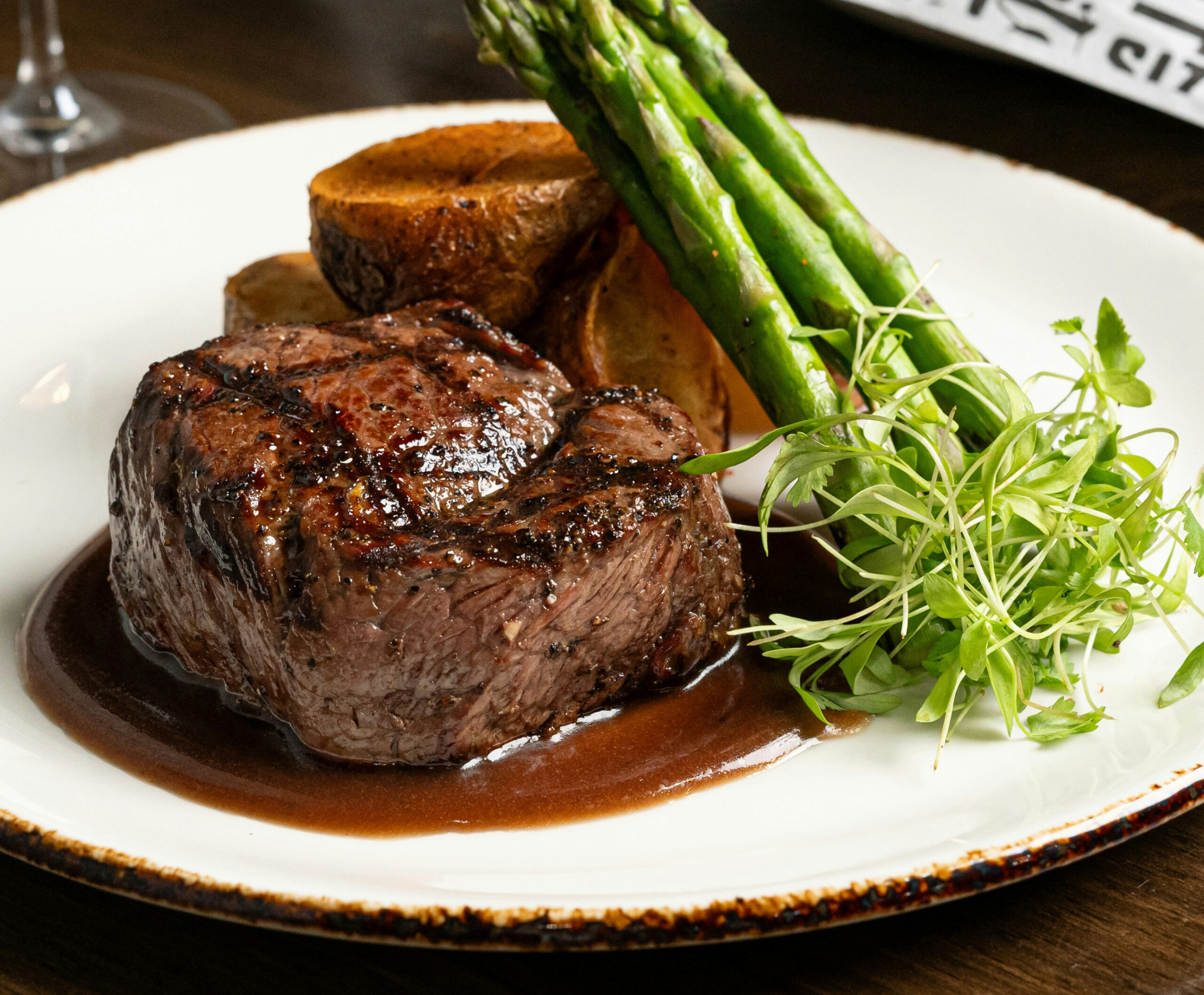 Close up of thick slab of grilled meat with chunks of potato and asparagus with greens