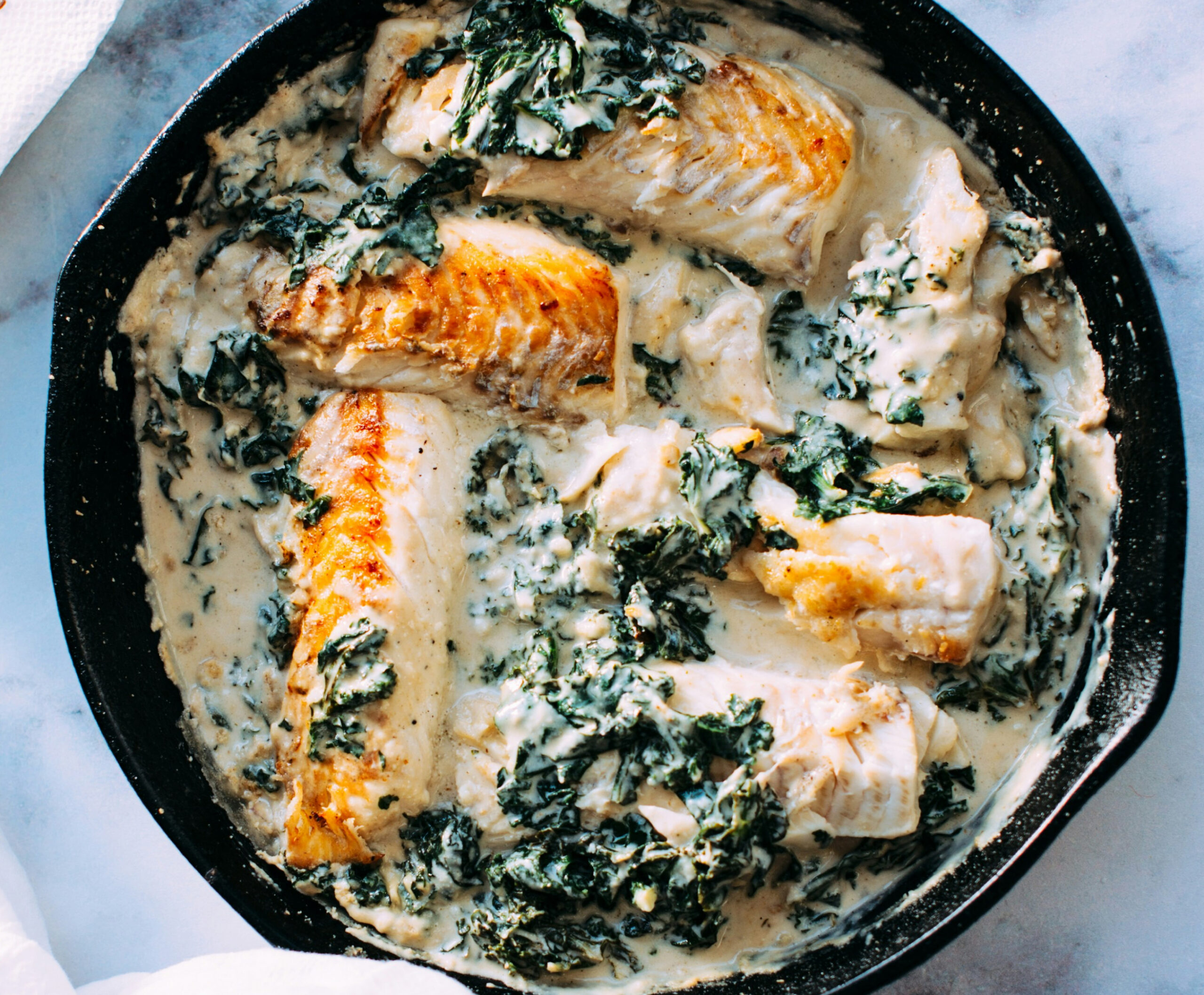 Close up of grilled fish in greens and white sauce in cast iron pan