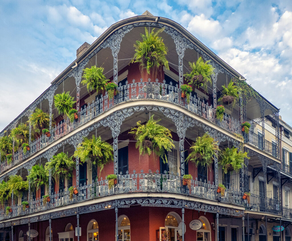 New Orleans corner brick building with ornate balconies and hanging ferns