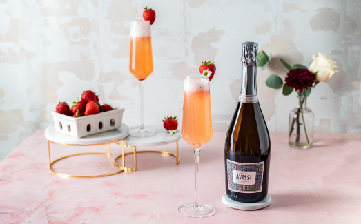 Table top arrangement of two mimosas, a container of strawberries, and a bottle of Avissi Prosecco