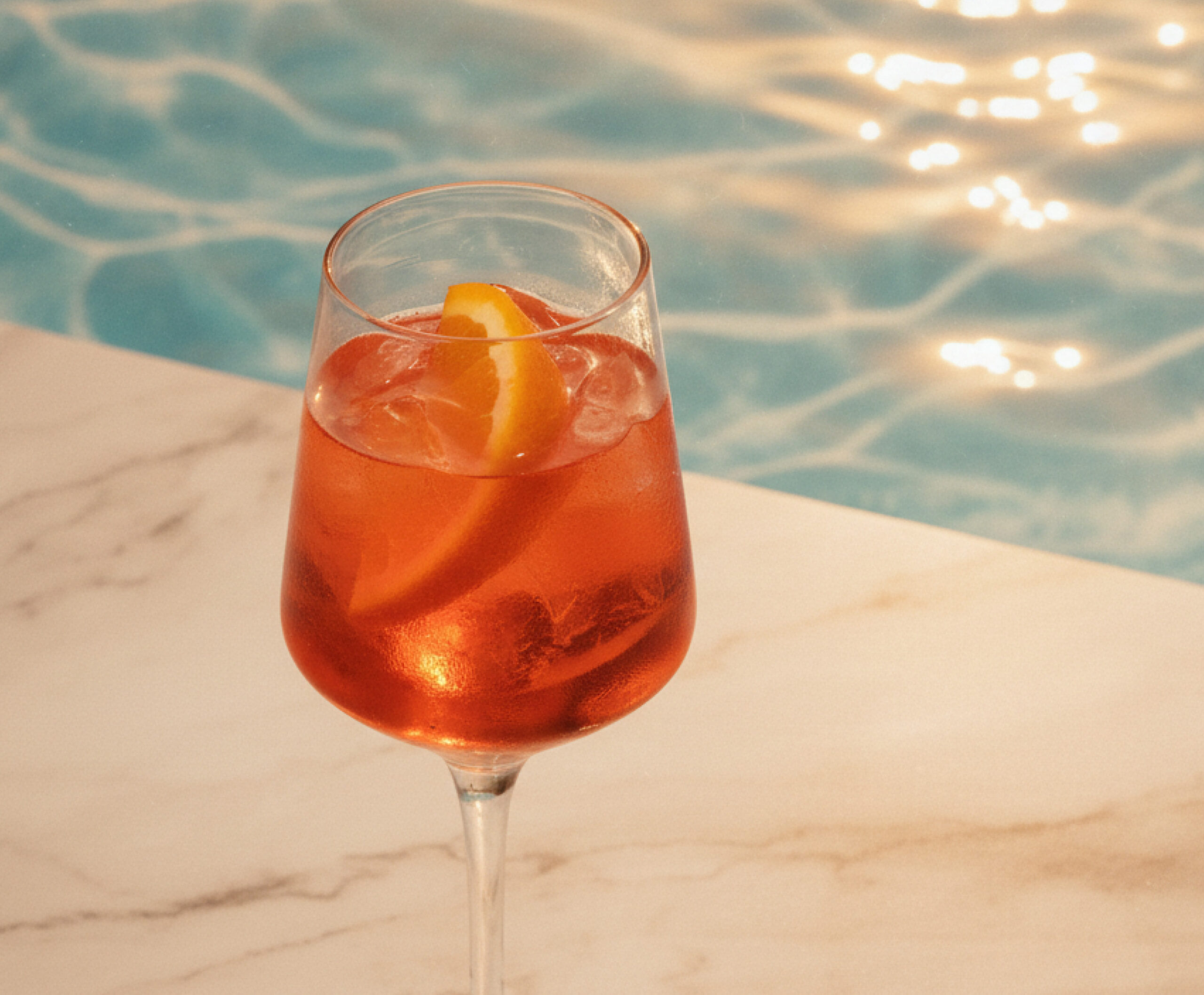 Close up of an aperol spritz cocktail in stemware on a marble surface with sparkling water in the background
