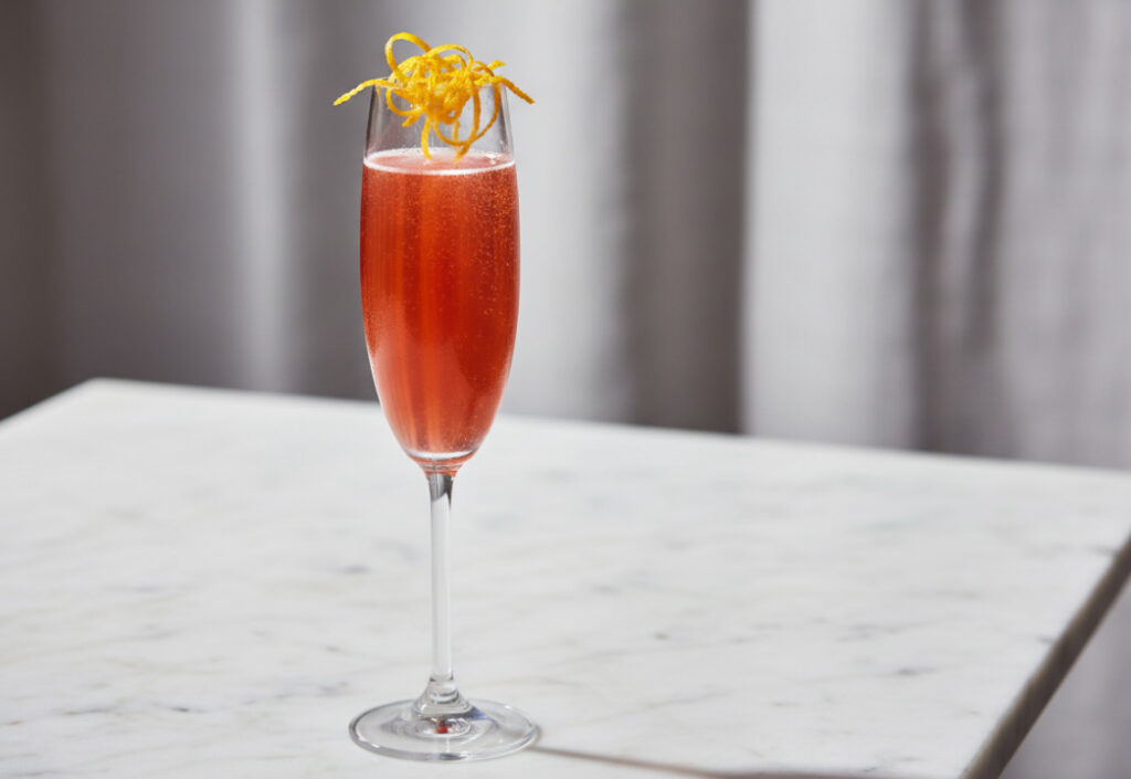 Close up of a cocktail in a champagne flute glass on a marble surface with blurred gray drapery in the background