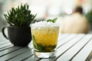 Rock glass filled with a prosecco cocktail with herb garnish on wood table